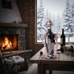 Une scène chaleureuse et hivernale mettant en vedette le porte-bouteille "Skieur" dans un décor de chalet de montagne.Il porte une bouteille de vin rouge qui fait office de "corps". Les détails en métal (skis, bâtons, gants et bonnet cuivré)