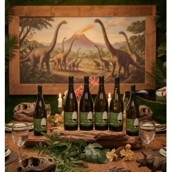Une table en bois est dressée avec des assiettes, des verres à vin et des couverts. La décoration est luxuriante, avec de la verdure, des fougères et des fleurs tropicales. Des crânes de dinosaures fossilisés.Six bouteilles de vin blanc Mauzac RHABDODON PRISCUS Terroir des Dinosaures sur une grande pièce de bois brut. Une main verse du vin dans un verre. Des bougies allumées sont dispersées sur la table. Un grand tableau encadré de bois est sur un mur couvert de verdure. La peinture représente un paysage préhistorique avec des dinosaures à long cou (sauropodes) errant dans une plaine, avec un volcan en éruption au loin.